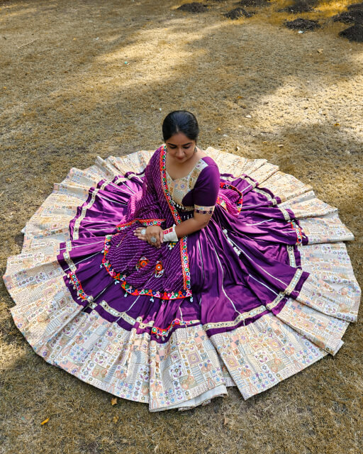 Woman wearing a royal purple chaniya choli with handcrafted Kutchi embroidery, custom-designed by Anokhi by Sneha boutique in Rajkot, sitting gracefully with the outfit beautifully spread in a circular layout on the ground.